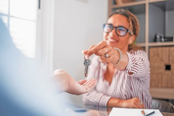 Smiling female realtor agent giving keys to apartment buyer. Homeowner receiving their new house key from a real estate agent at office. Happy saleswoman giving house keys to customer